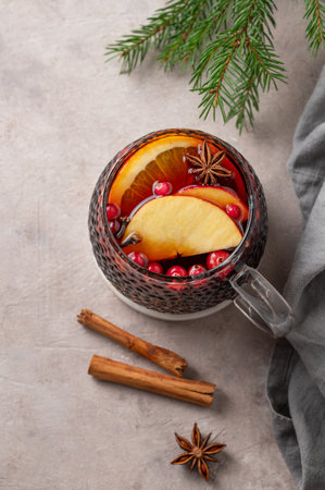 A cup of red mulled wine with spices, orange, apple slices and cranberry on a light background with cinnamon sticks and fir branch. A traditional autumn or Christmas drink concept for the holidays. Top view, copy space.の写真素材