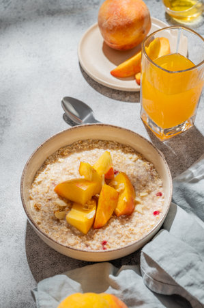 Oatmeal with peaches and nuts  in a bowl on a gray background with honey, glass of orange juice and morning shadows. Concept for a healthy vegan dish or breakfast snack. Top view, copy space.の写真素材