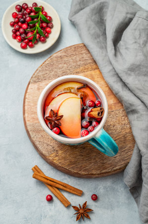 A mulled wine in a mug with cinnamon, cranberry and fruits on a wooden board on a light background with berries. A traditional warming punch or Christmas drink with orange, apples, and spice. Top view, copy space.の写真素材