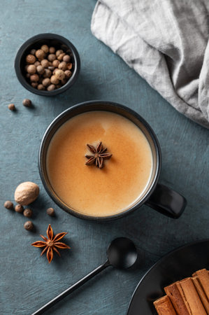Traditional Indian masala chai tea with milk and spices in a black cup on a dark background with spoon and napkin. A cozy hot drink concept for a menu or banner ad for an ethnic cafe or restaurant. Top view.の写真素材