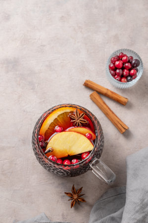 A cup of red mulled wine with spices, orange, apple slices and cranberry on a light background with cinnamon sticks. A traditional autumn or Christmas drink concept for the holidays. Top view, copy space.の写真素材