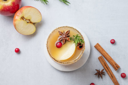 Apple cider with cinnamon, anise, brown sugar and rosemary in a glass on a light background with fresh fruits, cranberry and herb. Concept a traditional, spicy, warming drink for fall and winter. Top view, copy space.の写真素材
