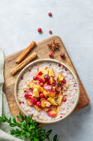 Overnight oatmeal with apple, cranberry and cinnamon in a plate on awooden board on a light background spice and branch. Concept for a healthy vegan meal for breakfast. Advertising menu or banner cafe. Top view, copy space.の写真素材