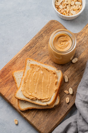 Peanut butter toast on a wooden board on a light background with scattered nuts, napkin and knife....