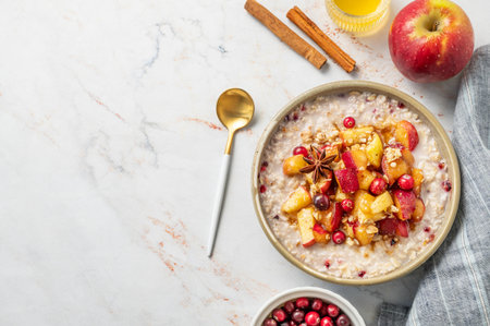 Flat lay of overnight oatmeal with apple, cranberry and cinnamon in a plate on a marble background with honey, spoon and napkin. Concept for a healthy vegan meal for breakfast. Advertising menu or banner cafe. Top view, copy space.の写真素材
