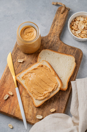 Peanut butter toast on a wooden board on a light background with nuts, knife and a napkin. Concept...