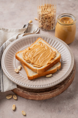 Peanut butter toast on a plate on a light background with scattered nuts, spread and napkin. Concept...