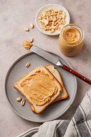 Peanut butter toast on a plate on a light background with scattered nuts, spread and napkin. Concept for a sweet vegetarian diet and healthy snacks for an American breakfast. Top view, copy space.の写真素材