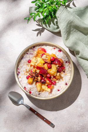 Overnight oatmeal with apple, cranberry and cinnamon in a bowl on a light background with spoon, branch and morning shadows. Concept for a healthy vegan meal for breakfast. Top view, copy space.の写真素材