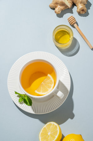 Hot tea with lemon, ginger, honey, and mint in a cup on a blue background with citrus fruits and morning shadows. A drink concept for supporting immunity and health. Advertising banner or cafe menu. Top view, copy space.の写真素材