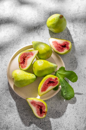 Sweet green figs in a plate a on a gray concrete background with leaves and sunlight. Concept of...
