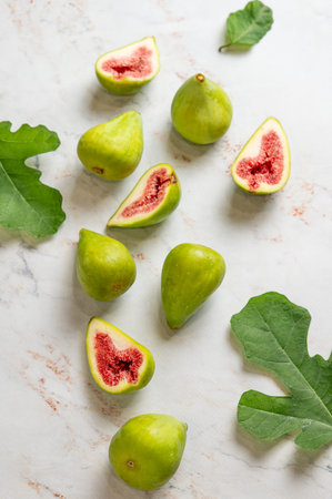 Flat lay of sweet green figs, sliced and leaves on a light marble background. Concept of juicy and healthy summer fruits. Top view, copy space.の写真素材