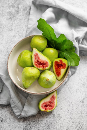Sweet green figs in a plate with leaves and napkin on a gray concrete background. Concept of juicy and healthy summer fruits. Top view, copy space.の写真素材