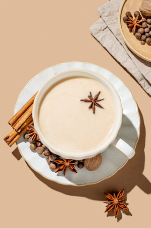 Traditional Indian masala chai tea with milk and spices in a cup on a beige background with cinnamon, anise and shadows. A cozy hot drink concept for a menu or banner for an ethnic cafe or restaurant. Top view, copy space.