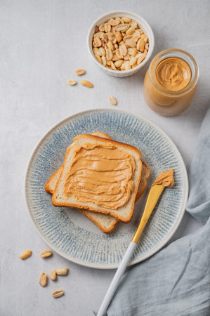 Peanut butter toast on a plate on a light background with nuts, napkin and knife. Concept of a...