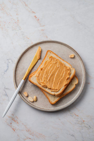 Peanut butter toast on a plate with knife on a light marble background. Concept of a nutritious...