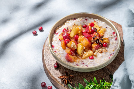 Overnight oatmeal with apple, cranberry and cinnamon in a bowl on a wooden board on a blue background with berry and morning shadows. Concept for a healthy vegan meal for breakfast. Advertising menu or banner cafe. Top view, copy space.の写真素材