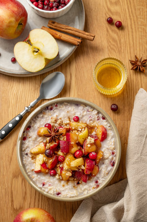 Overnight oatmeal with apple, cranberry and cinnamon in a plate on a wooden background with honey, spice and fruit. Concept for a healthy vegan meal for breakfast. Top view.の写真素材