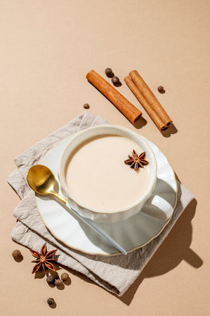 Traditional Indian masala chai tea with milk and spices in a cup on a beige background with cinnamon, anise and shadows. A cozy hot drink concept for a menu or banner for an ethnic cafe or restaurant. Top view, copy space.の写真素材