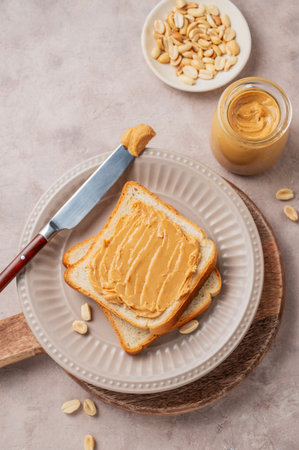 Peanut butter toast on a plate on a light background with scattered nuts, spread and knife. Concept for a sweet vegetarian diet and healthy snacks for an American breakfast. Top view, copy space.の写真素材