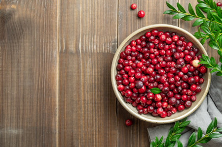 Fresh cranberries in a dark bowl on a wooden background with green branch and napkin. Concept of healthy natural wild berries in rustic style for advertising banner. Top view, copy space.の写真素材