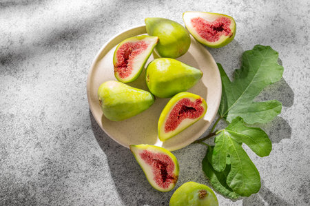 Sweet green figs in a plate a on a gray concrete background with leaves and sunlight. Concept of juicy and healthy summer fruits. Top view, copy space.の写真素材