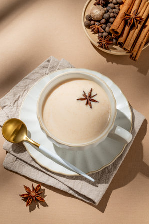Traditional Indian masala chai tea with milk and spices in a cup on a beige background with cinnamon, anise and shadows. A cozy hot drink concept for a menu or banner for an ethnic cafe or restaurant. Top view, copy space.の写真素材