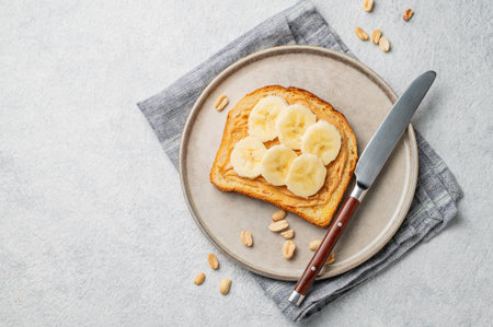 Peanut butter toast and banana in a plate on a light background with napkin and knife. Concept for nutritious and healthy snacks for an American breakfast. Top view, copy space.の写真素材