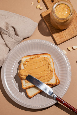 Peanut butter toast on a plate on a beige background with a knife, napkin and shadow. Concept of nutritious and healthy snacks for an American breakfast. Top view,  copy space.の写真素材