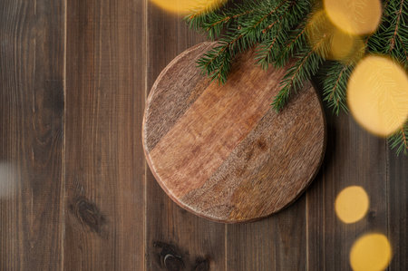 Fir branches and Christmas lights with a bokeh effect on a dark wooden background with a product display podium. A festive illumination and decor concept for a New Year's advertisement or banner. Top view, copy space.の写真素材