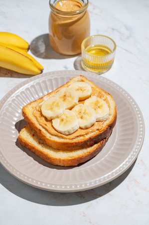 Peanut butter sandwich and banana on a plate on a marble background with fruits and honey. Concept for nutritious and healthy snacks for breakfast.の写真素材