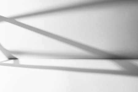 Geometric shadows cast on white background. Minimalist photography style and a concept of contrast and elegance for product showcases or creative designs with space for text. Front view.の写真素材