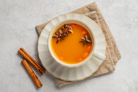 Sea buckthorn herbal tea in a cup on a light background with spices and napkin. Concept for a hot autumn organic drink to boost immunity. Top view, copy space.の写真素材