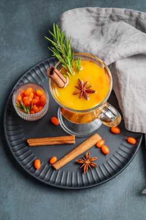 Sea buckthorn herbal tea in a glass on a black plate on a dark background with berries, spices and napkin. Concept for a hot autumn organic drink to boost immunity. Top view, copy space.の写真素材