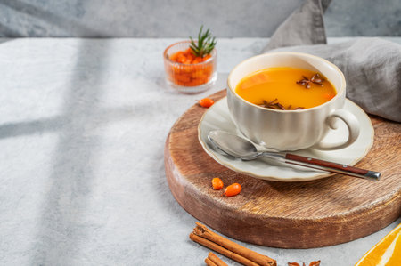 Sea buckthorn herbal tea in a cup on a wooden board on a light background with spices, berries and morning shadows. Concept for a hot autumn organic drink to boost immunity. Front view, copy space.の写真素材