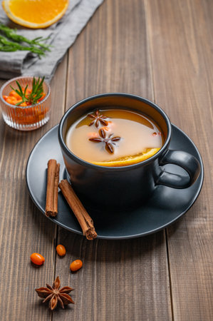 Sea buckthorn herbal tea in a black cup on a wooden background with spices, berries, herb and napkin. Concept for a hot autumn organic drink to boost immunity in rustic style. Top view, copy space.の写真素材