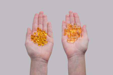 Hands holding two types of yellow softgel capsules containing D3 and Omega on a light  background. Concept for health, vitamins, or dietary supplements. Top view, copy space.の写真素材