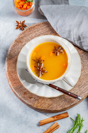Sea buckthorn herbal tea in a cup on a wooden board on a light background with spices, berries and morning shadows. Concept for a hot autumn organic drink to boost immunity. Top view, copy space.の写真素材