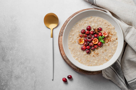 Oatmeal with cranberry, cinnamon and spicy in a plate on a gray concrete background with fresh...