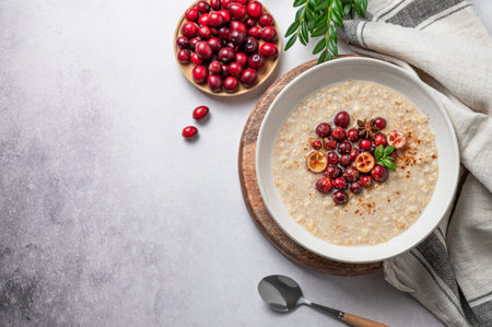 Oatmeal with cranberry, cinnamon and spicy in a plate on a gray concrete background with fresh berry, spoon and napkin. Concept for a healthy vegan porrige for breakfast. Top view, copy space.の写真素材