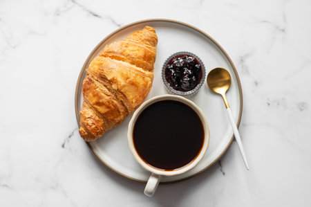 Cup of espresso coffee and fresh croissant on a light marble background with berry jam and spoon. Creative and concept of delisious food and french breakfast for advertising banner menu cafe. Top view, copy space.