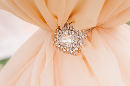 Diamonds and silver brooch on peachy satin as a backgroundの写真素材