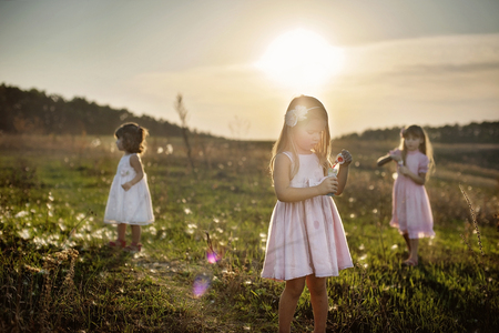 Three little girls at the green field in sunset time, with bubblesの写真素材
