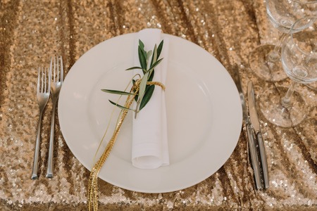 Table appointments of a holiday table. The white napkin decorated with gold thread and a branch of an eucalyptusの写真素材