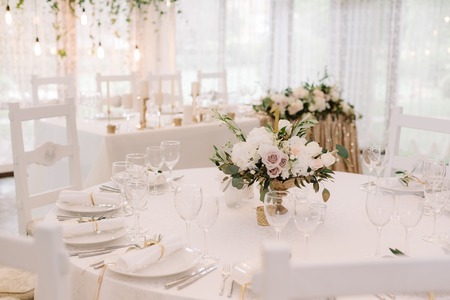 Round white table with graceful compositions of fresh flowers. A decor of wedding tables at restaurantの写真素材