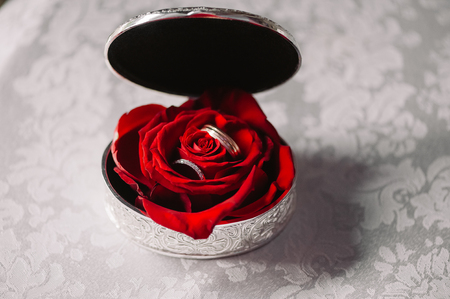 Wedding silver box with the rings in the red rose on the white tableclothの写真素材