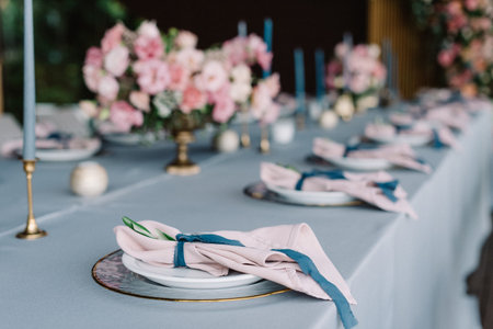 Stylish and beautiful wedding table service with blue tablecloth, festive dishes and gentle pink...