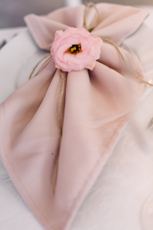 A little eustoma bud decorates a cloth napkin on a dinner plate. Wedding table service for reception of guestsの写真素材