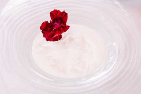 White sauce in a glass plate. A bright natural flower adorns a plate with white puree. Original...