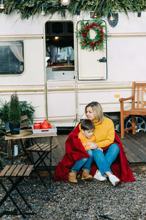 Beautiful mother and child boy with red plaid sitting near trailer. Family vacation RV holiday trip, happy smiling family travel on camper, people in motorhome interior. Caravan in parkの写真素材
